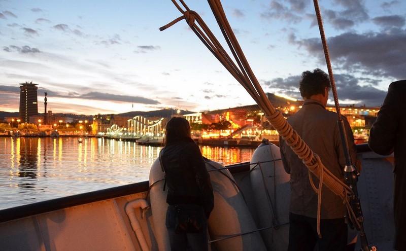 Una persona a bord del vaixell contempla la posta de sol sobre Barcelonaof a body of water