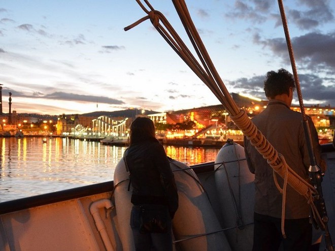 a person standing in front of a body of water on Barcelona harbor with the sunset lights