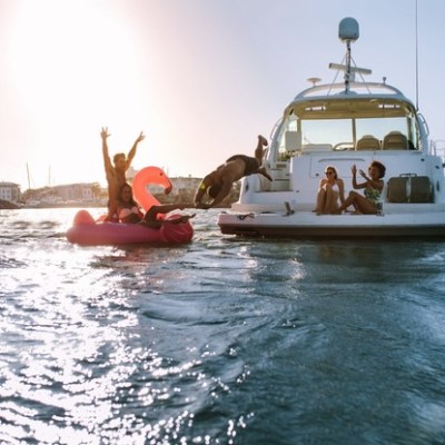a group of people on a boat in the water, having a party. Man diving in the sea with friends cheering from yacht and inflatable toy.