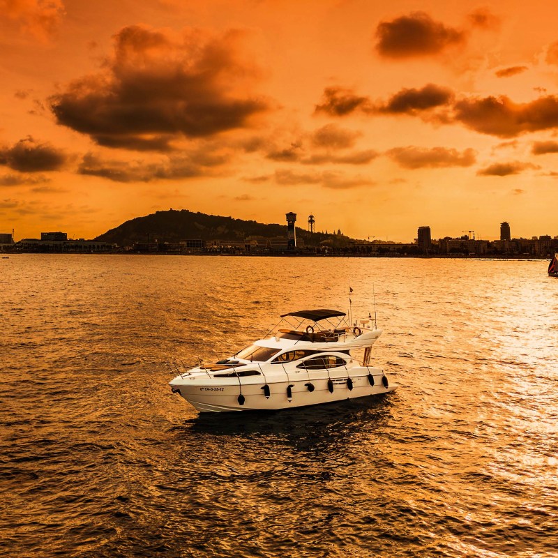Boat on water with orange sunset and city skyline in background.