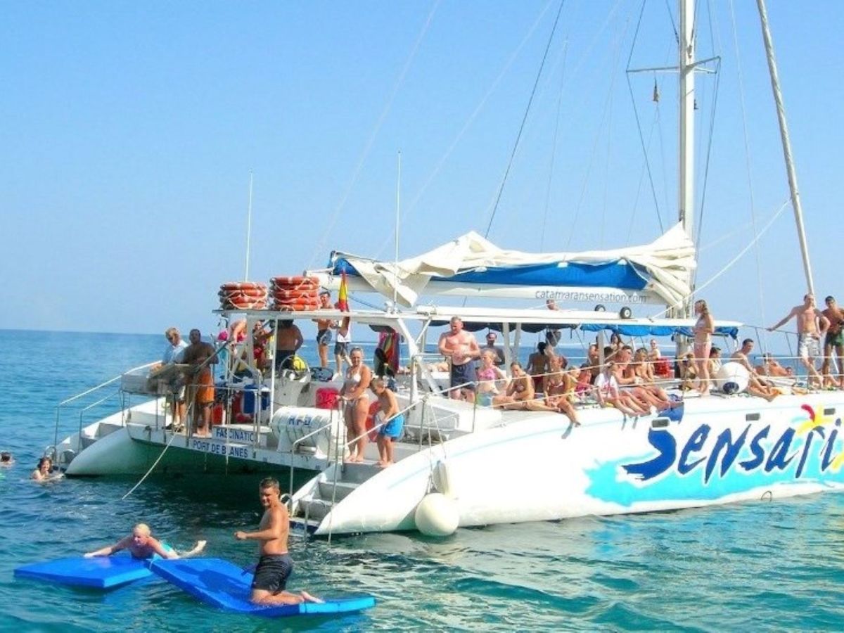 People enjoying water activities around a large catamaran in the ocean.