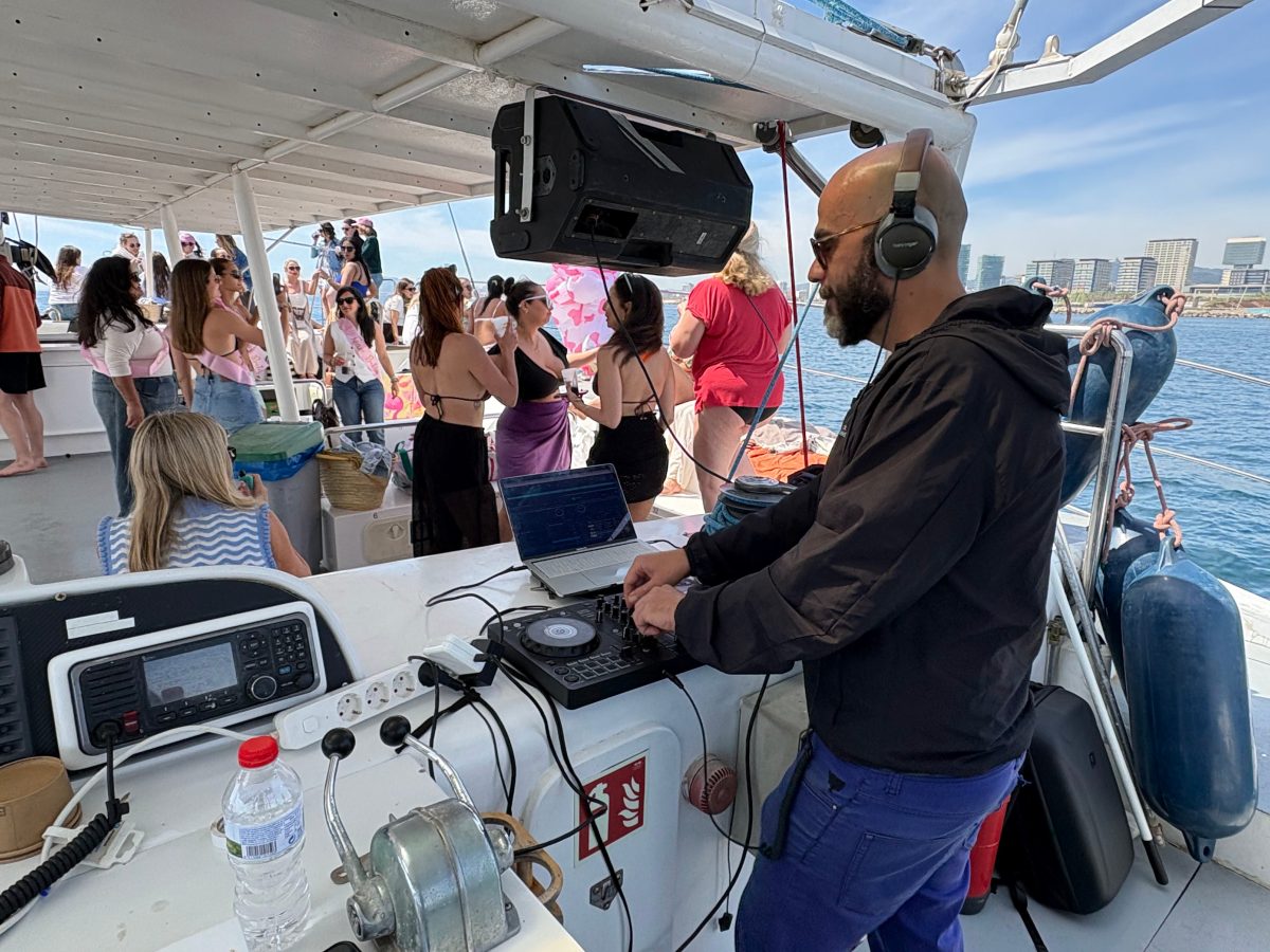 DJ playing music on a boat with partygoers in the background.